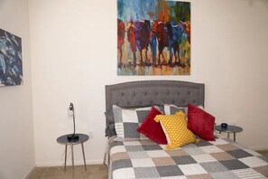 Cozy retreat with a large bed, checkered bedspread, and a vibrant painting above.