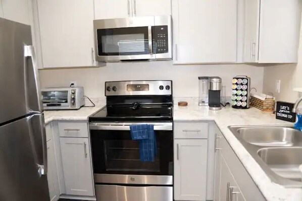 Compact kitchen with modern appliances, stainless steel sinks, and a white counter.