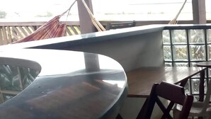 Una habitación con un ventanal grande, barandilla metálica, mesa de madera y una silla.