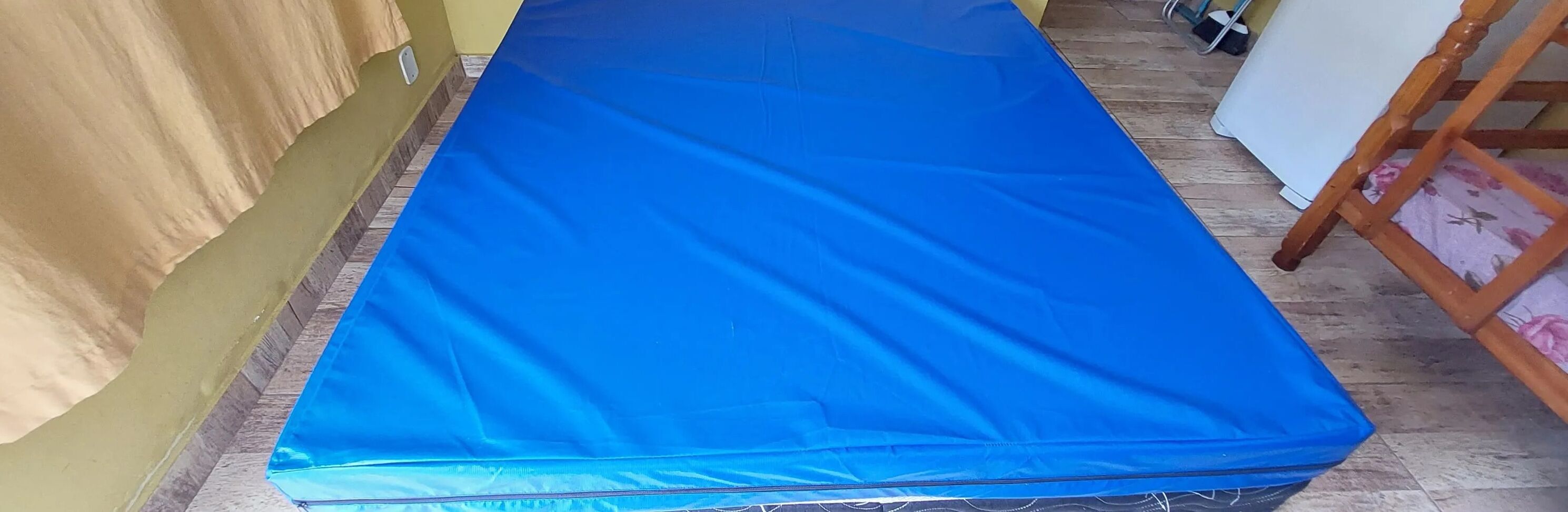 Une pièce avec un matelas bleu posé sur le sol, une chaise en bois et un mur blanc.