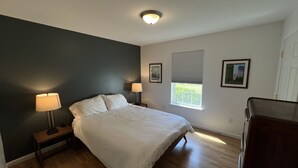A bedroom with a bed, two bedside tables, a nightstand, a window with blinds, and two wall-mounted lamps. - Relaxing 2 bedroom home minutes away from PMRP (Beattyville)