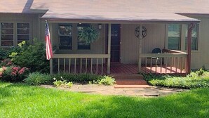 Una casa de un piso con porche delantero, una pequeña terraza y una bandera.