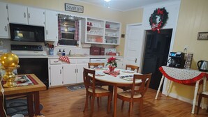Una cocina con armarios blancos, microondas, lavamanos y comedor con mesa y sillas.