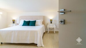 A neatly made bed with white bedding and teal pillows, two bedside tables with lamps, and a wall-mounted shelf. - Villa Vittoria  - Dimora fronte mare (Augusta)