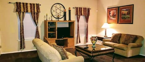 A living room with a sofa, armchair, coffee table, TV stand, and curtains.