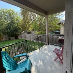 A covered porch with a grill, two chairs, and a view of a backyard with a fence and trees. - Beautiful large home near Sea World,  Riverwalk, Fiesta Texas  (San Antonio)