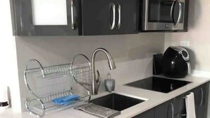 A modern kitchen with dark cabinets, a white countertop, a stainless steel sink, a microwave, and a dish rack.