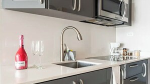 A modern kitchen with a stainless steel sink, a wine bottle, and two glasses on the counter.
