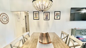 Ein Essbereich mit einem Holztisch, Stühlen, einer Chandelier und gerahmten Kunstwerken an der Wand.