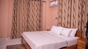 A bedroom with a bed, curtains, a nightstand, and a wall-mounted air conditioner. - Executive 3-bed Furnished Apartment in Kwashieman (Accra)