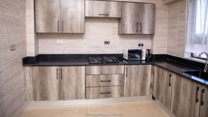 A modern kitchen with wood cabinets, a black countertop, a stove, and a microwave. - Executive 3-bed Furnished Apartment in Kwashieman (Accra)