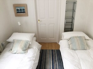 Une chambre avec deux lits, une porte, un tableau encadré au mur et une étagère en métal.