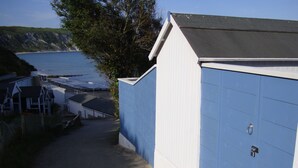 En smal sti, der fører til en blå bygning med en hvid dør, beliggende ved kysten med klipper og en strand.