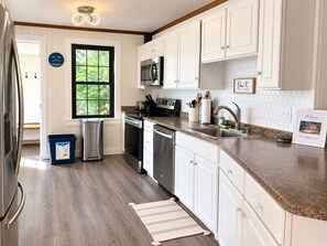 A modern kitchen with white cabinetry, stainless steel appliances, and a large window. - Luxury Lakefront Retreat - Private Beach, Dock & Cozy She Shed (Sandown)