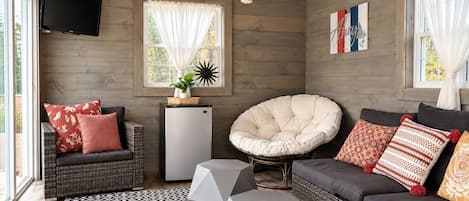 A cozy room with a wooden ceiling, a television, a refrigerator, a comfortable chair, a sofa, and a patterned rug.