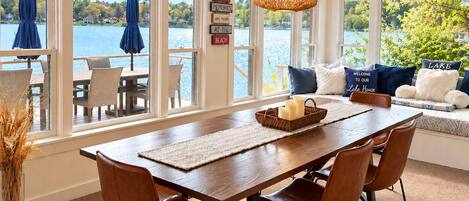 A dining area with a wooden table and chairs, large windows with a view of a lake, and a hanging light fixture.