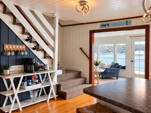 A staircase with a coffee station, a sign reading 'Home is where the anchor drops,' and a view of a body of water through a door. - Luxury Lakefront Retreat - Private Beach, Dock & Cozy She Shed (Sandown)