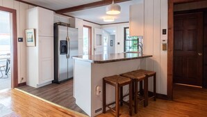 A kitchen with a central island, wooden stools, a refrigerator, and a water dispenser.