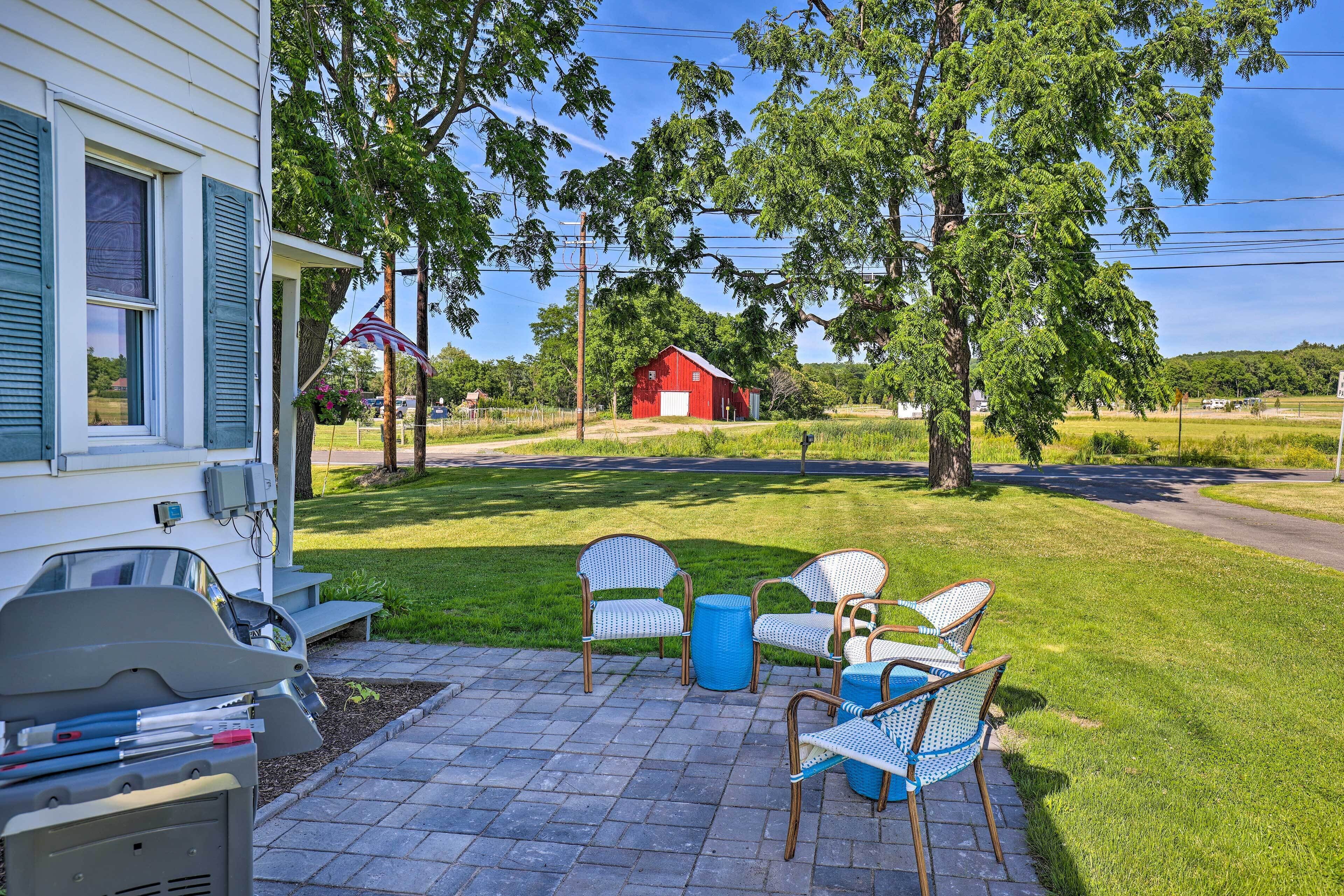 Un patio con mobiliario exterior, una parrilla de barbacoa y un granero rojo al fondo.