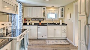 Eine moderne Küche mit weißen Schränken, einem Einbauofen, einer Spülmaschine und einem Fenster mit Vorhang.