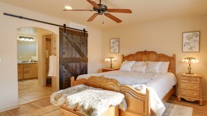 Un dormitorio con cama de madera, un banco, ventilador de techo y mesita de noche con lámpara.