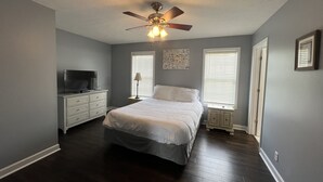 Quarto com cama, ventilador de teto, televisão e janela com persianas.