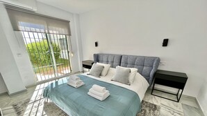 A modern bedroom with a large bed, a nightstand, a window with a view of greenery, and a sliding door. - 6 -  Sea view apartment in Calahonda (Mijas Costa)