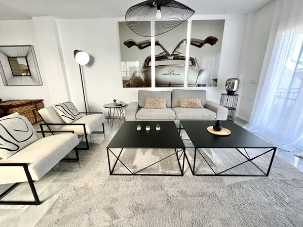 A modern living room with a sofa, two black coffee tables, a floor lamp, and a large Mercedes-Benz poster on the wall.