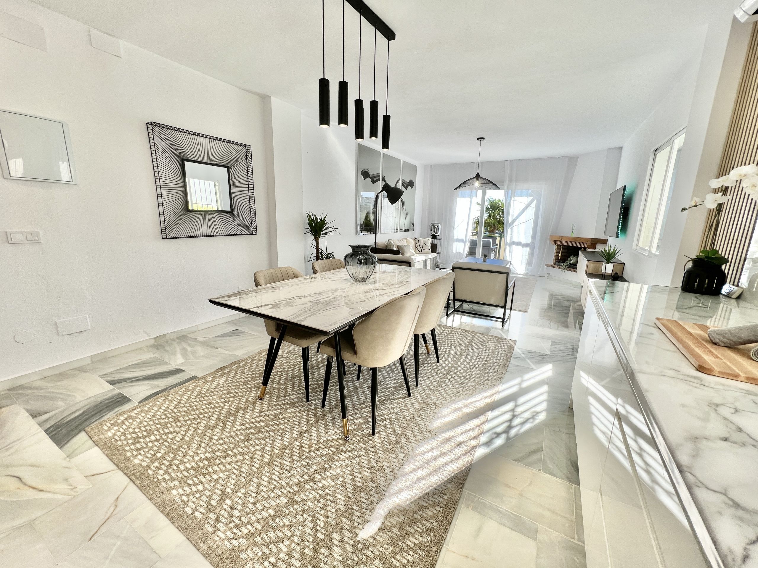A modern dining area with a marble table, beige chairs, and a patterned rug.