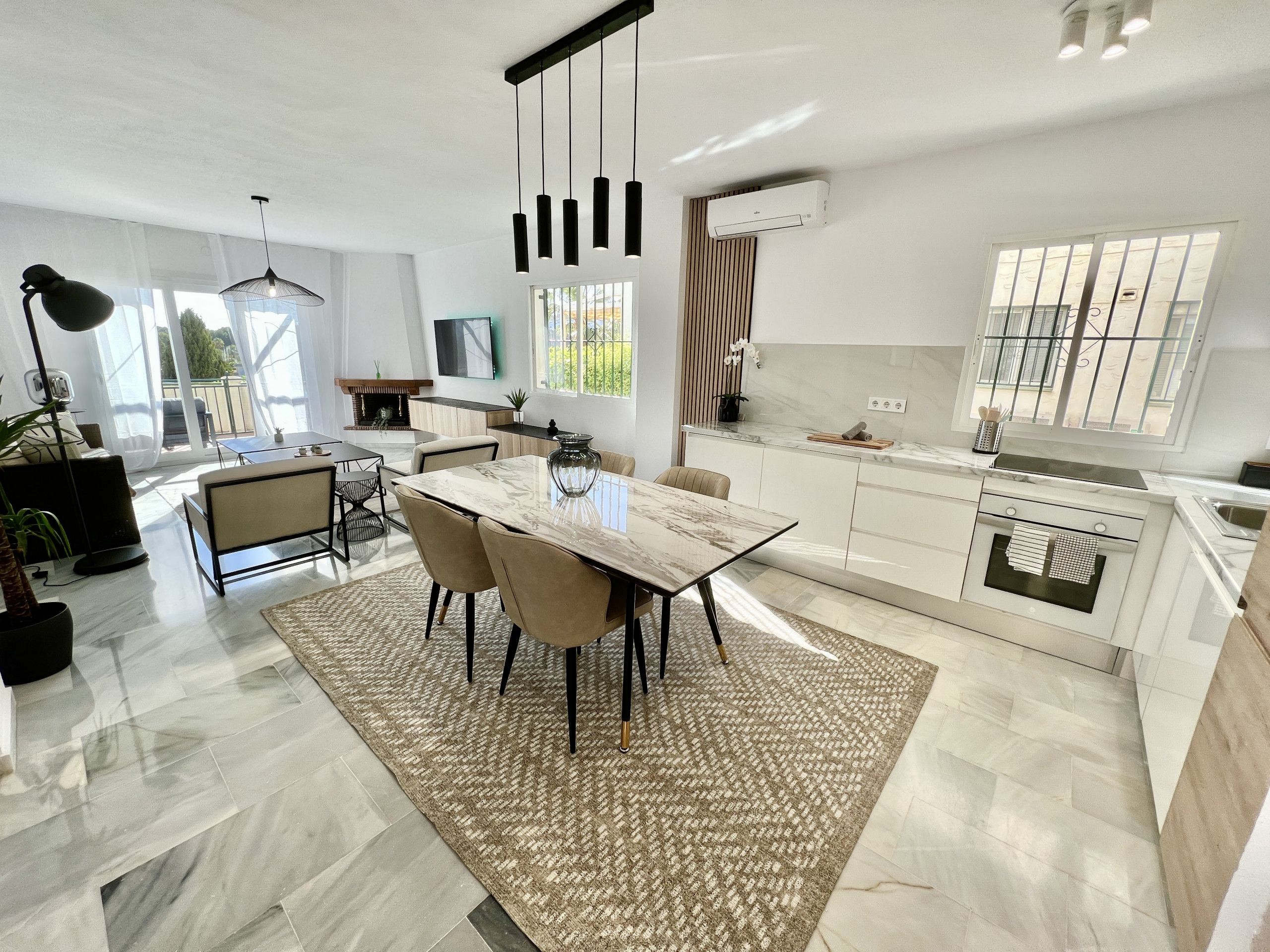 A modern kitchen with a marble countertop, a dining area with a glass-top table, and a large window providing natural light.