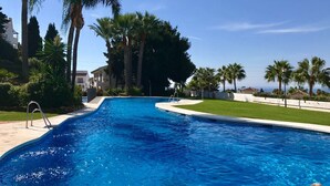 A swimming pool with a clear blue water, surrounded by palm trees and a white building in the background. - 6 -  Sea view apartment in Calahonda (Mijas Costa)