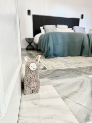 A plush toy on a marble floor, a bed with a dark headboard, and a green bedspread in a bedroom.