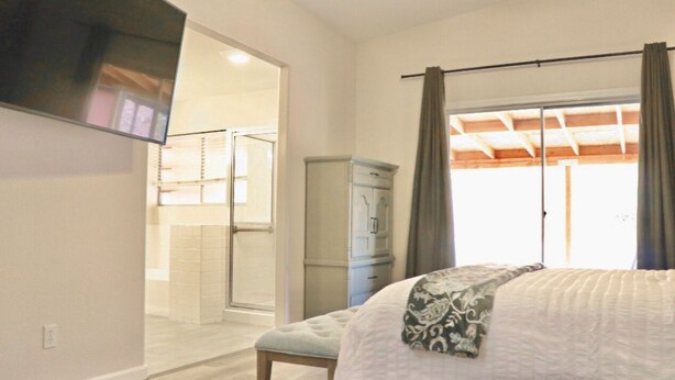 A bedroom with a bed, a wardrobe, a television mounted on the wall, and a bathroom visible through an open door.