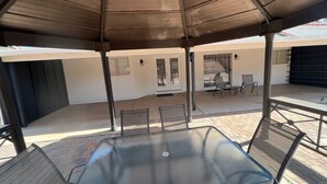 An outdoor patio area with a glass table and chairs, a covered seating area, and a view of the building's interior.