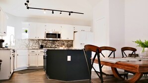 A modern kitchen with white cabinets, a black island, and a dining area with wooden chairs and a table.