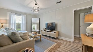 A living room with a sofa, coffee table, TV, and a bookshelf. - Enjoy our cozy cottage just minutes from A&M Campus (Bryan)