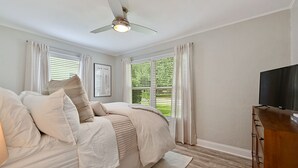 A bedroom with a bed, a ceiling fan, a TV, and a window with blinds. - Enjoy our cozy cottage just minutes from A&M Campus (Bryan)