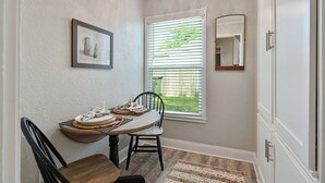 A dining area with a wooden table, chairs, a framed picture, and a window with blinds. - Enjoy our cozy cottage just minutes from A&M Campus (Bryan)