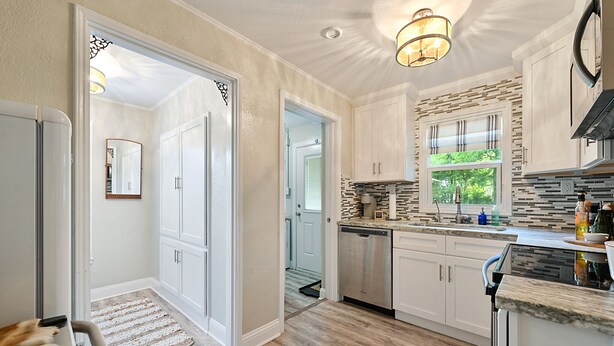 A modern kitchen with white cabinetry, a stone backsplash, and a built-in dishwasher. - Enjoy our cozy cottage just minutes from A&M Campus (Bryan)