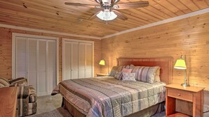 Een slaapkamer met een houten plafond, een bed met beddengoed met een patroon, twee bedlampjes en een nachtkastje met een lade.