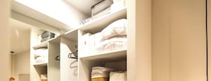 Ein ordentlich eingerichteter Kleiderschrank mit Regalen und Kleiderstangen, gefĂŒllt mit sauber zusammengefalteter Kleidung und einigen Kisten.