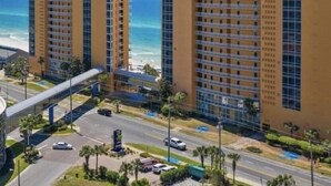 Een hoog hotelgebouw met meerdere verdiepingen, uitzicht op het strand en een voetgangersbrug naar de weg.