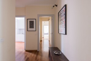 A hallway with a wooden floor, a framed abstract artwork, a framed alphabet poster, and a small table with a bowl.