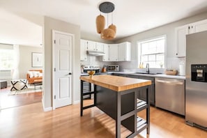 A modern kitchen with white cabinets, a wooden island, stainless steel appliances, and a hanging light fixture. - Spacious Lake Community House near Hudson (Athens)