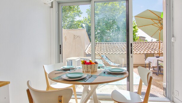 A dining area with a table set for two, chairs, and a view of a tiled roof and greenery outside. - Appartement Pompidou - Welkeys (La Seyne-sur-Mer)