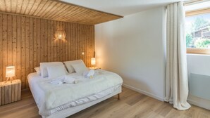 A bedroom with a wooden ceiling, a bed with white linens, two bedside lamps, and a view of greenery outside.