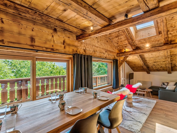 Un intérieur en bois avec une table à manger pour deux personnes, de grandes fenêtres et une vue sur la verdure environnante.
