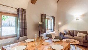 A dining area with a wooden table set for four, a sofa, and a TV mounted on the wall.