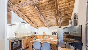 A modern kitchen with wooden beams, a dining area with chairs, and a built-in oven.