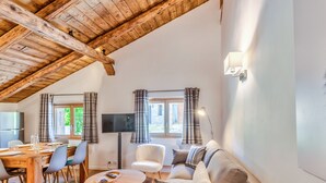 A cozy living room with a wooden ceiling, a sofa, a TV, and a dining area with a table and chairs.
